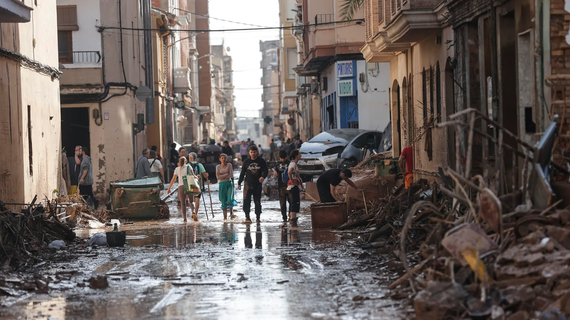 Varias personas caminan entre el lodo acumulado en las calles de Catarroja a causa de las intensas lluvias caídas por la DANA.