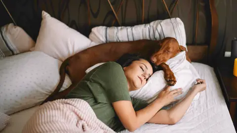 Una mujer durmiendo en la cama con su perro Una mujer durmiendo en la cama con su perro