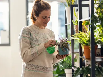 Una mujer regando las plantas con los auriculares puestos Una mujer regando las plantas con los auriculares puestos