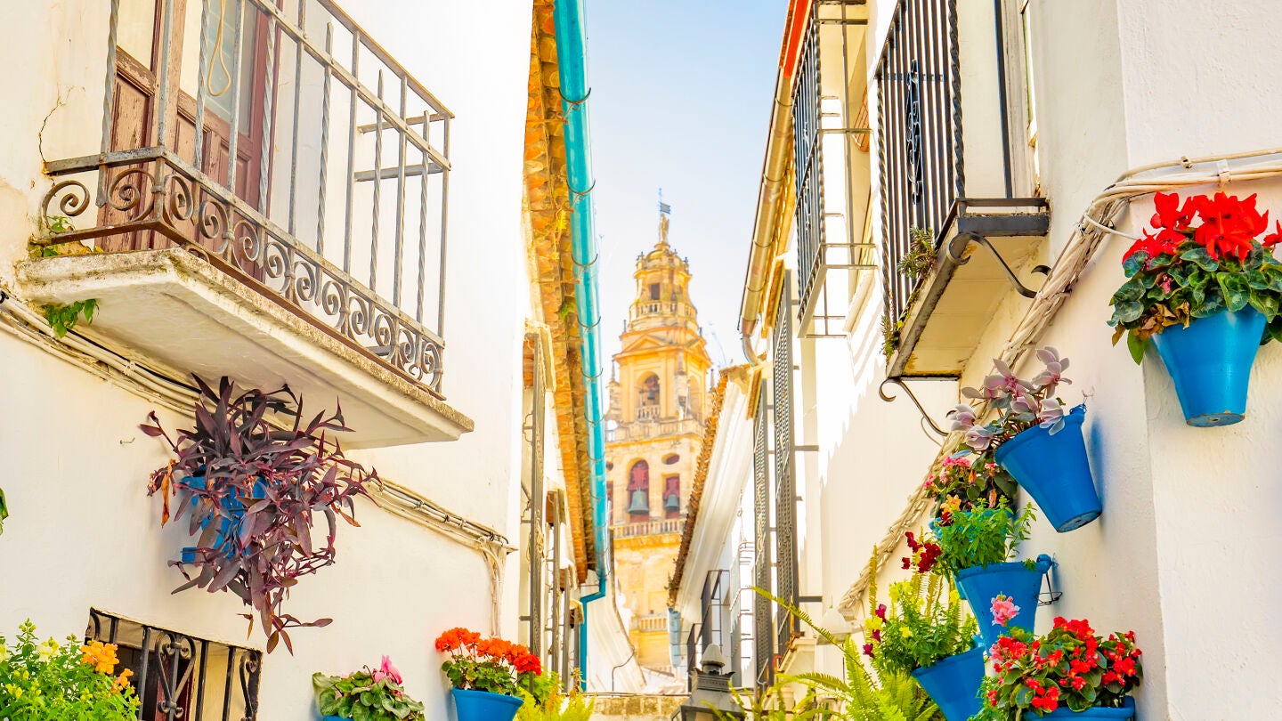Una calle de C&oacute;rdoba llena de flores con la torre de la Catedral de la Mezquita de fondo