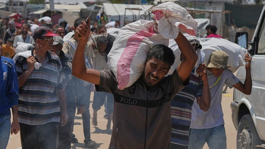 Un hombre carga con sacos de comida cerca de un punto de distribución de ayuda en Rafah Un hombre carga con sacos de comida cerca de un punto de distribución de ayuda en Rafah