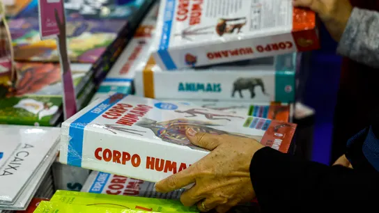 Ya se puede solicitar el Bono Cultural Joven: cómo hacerlo, quién puede solicitarlo y cuánto dinero corresponde Una mano agarrando un libro y de fondo muchos más libros