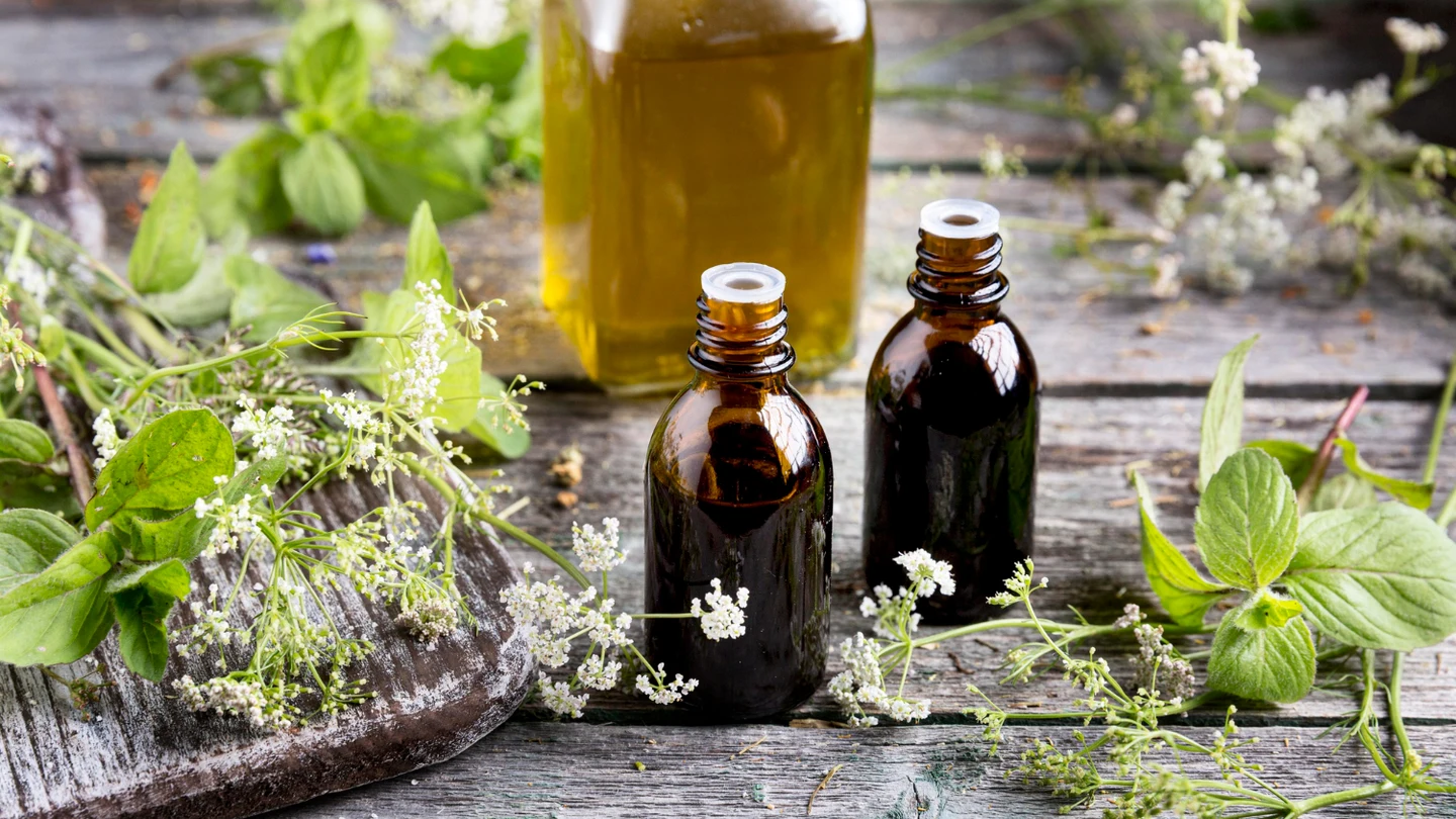 Beneficios, remedios y características de la hierba de San Juan como remedio natural. Dos frascos de cristal marrón preparados con hierba de San Juan como remedio natural reposan sobre una mesa, rodeados de plantas silvestres.