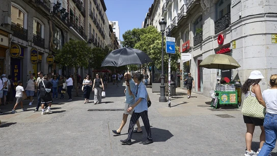 Dos personas caminan por la Puerta del Sol de Madrid con paraguas para aplacar el sol. Dos personas caminan por la Puerta del Sol de Madrid con paraguas para aplacar el sol.