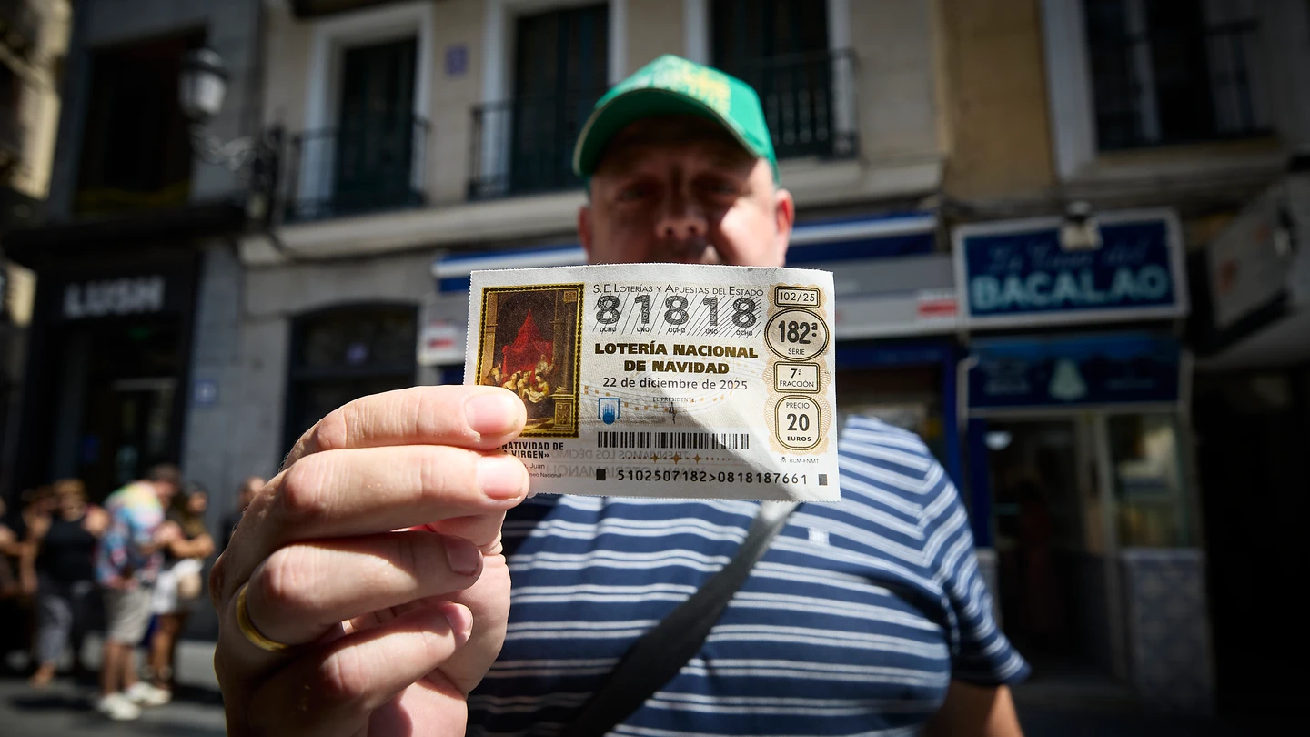 Un hombre enseña orgullosos su décimo de la Lotería de Navidad de 2025 comprado en Doña Manolita. Un hombre con gorra y camiseta de rayas enseña orgullosos su décimo de la Lotería de Navidad de 2025 comprado en Doña Manolita, a las puertas de la administración.