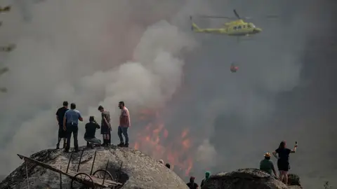 Varias personas observan la labor de un helicóptero de extinción del incendio forestal en Avión (Ourense) Varias personas observan la labor de un helicóptero de extinción del incendio forestal en Avión (Ourense)