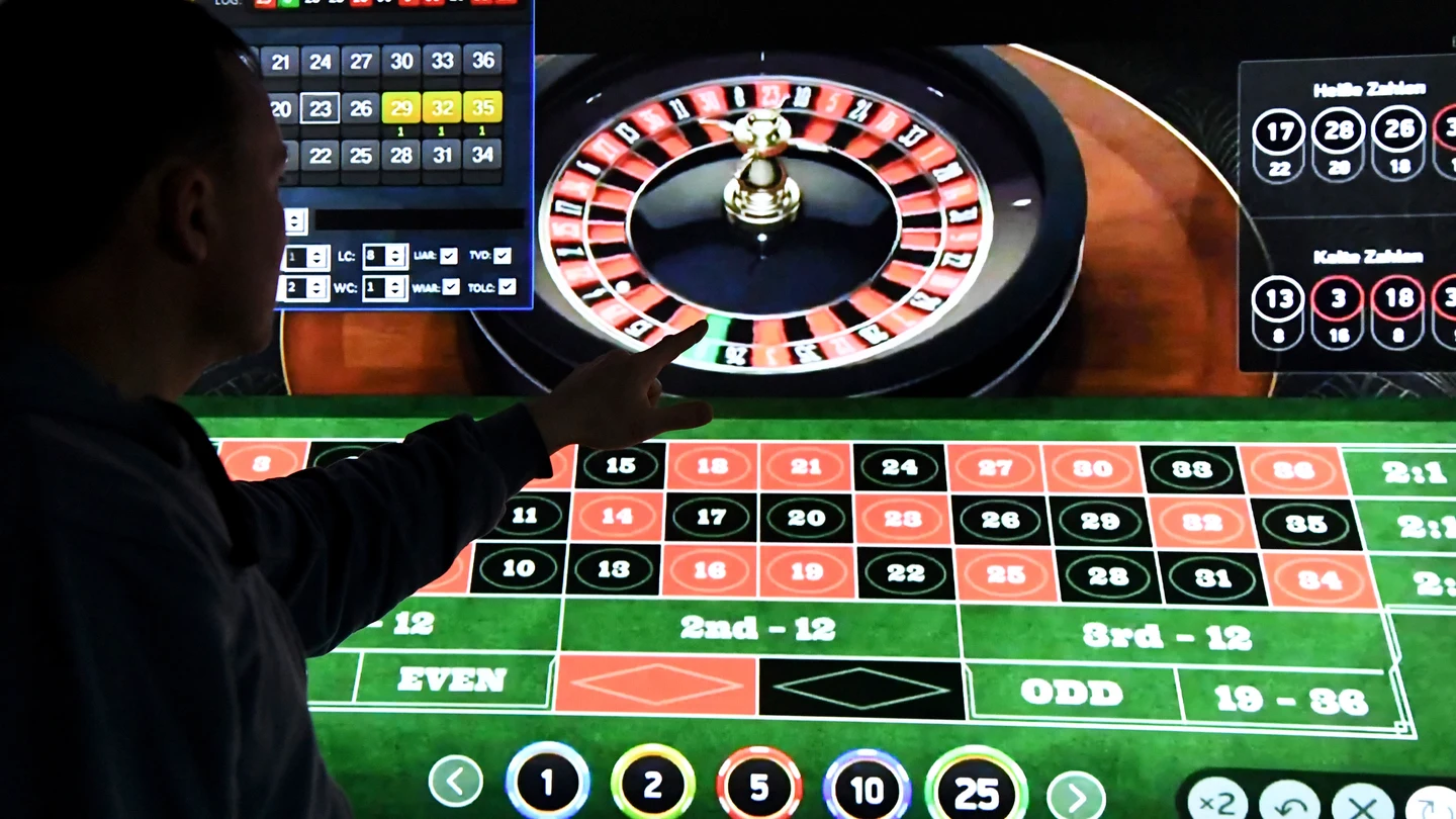 Un hombre está de pie frente a una pantalla con una página de ruleta online. Un hombre está de pie frente a una pantalla con una página de ruleta online.