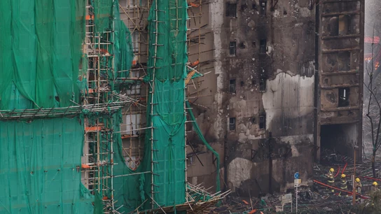Los bomberos pasan junto a andamios de bambú carbonizados en el complejo en Hong Kong Los bomberos pasan junto a andamios de bambú carbonizados en el complejo en Hong Kong