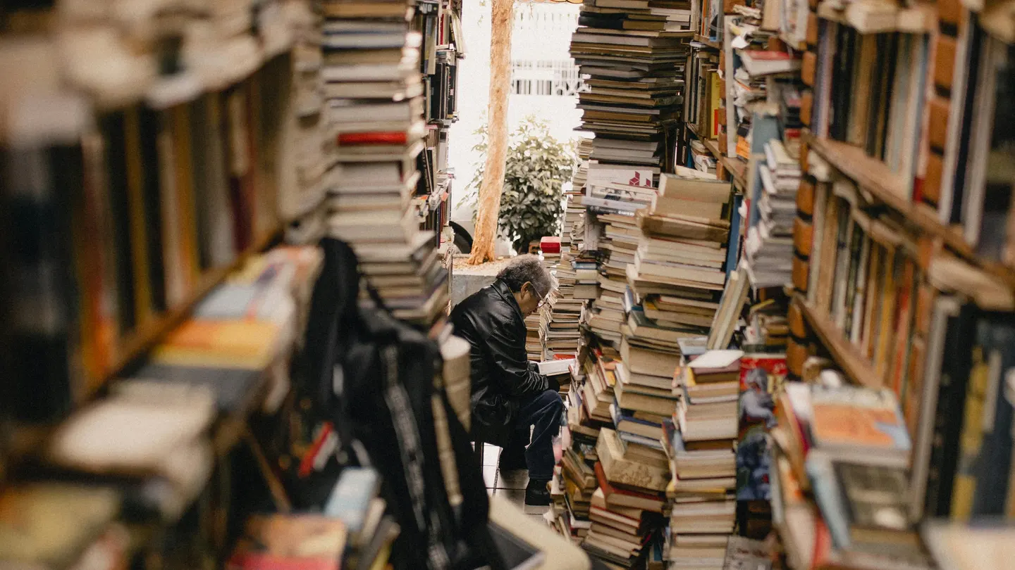 Un hombre hojea un libro en una librería repleta Un hombre hojea un libro en una librería repleta