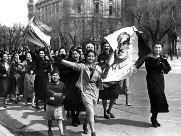 Un grupo de muchachas recorren alegres las calles de Madrid, con un retrato de Franco y la bandera nacional.