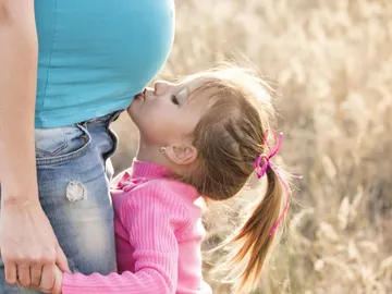 Una niña besando la barriga embarazada de su madre Una niña besando la barriga embarazada de su madre