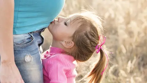 Una niña besando la barriga embarazada de su madre Una niña besando la barriga embarazada de su madre