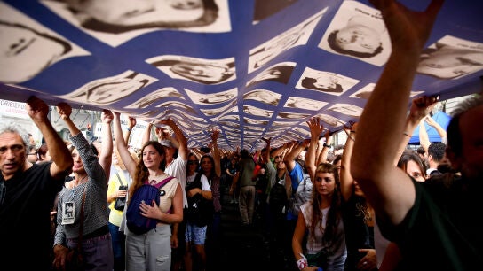 Manifestantes marchan bajo una pancarta con retratos de personas desaparecidas