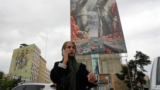 Una mujer habla por teléfono mientras pasa junto a una valla que muestra a Rais Ali Delvari, héroe nacional iraní, y al difunto jefe de la marina de la Guardia Revolucionaria, Alireza Tangsiri Una mujer habla por teléfono mientras pasa junto a una valla que muestra a Rais Ali Delvari, héroe nacional iraní, y al difunto jefe de la marina de la Guardia Revolucionaria, Alireza Tangsiri