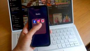 Una persona con un m&oacute;vil donde se ven logos de varias redes sociales.