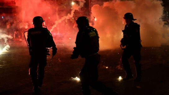 Agentes de polic&iacute;a se protegen de las bengalas tras la victoria del Paris Saint-Germain en la Liga de Campeones de la UEFA.