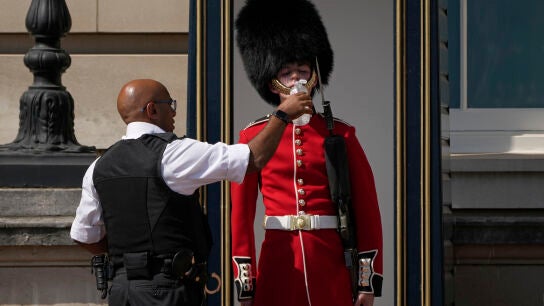 Un agente de polic&iacute;a da agua a un soldado brit&aacute;nico que est&aacute; de guardia frente al Palacio de Buckingham, durante una jornada de calor en Londres.