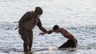 Un soldado del ej&eacute;rcito ayuda a un inmigrante a su llegada a la playa de El Tarajal en Ceuta.