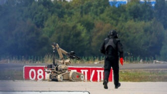 Un agente de polic&iacute;a con traje de protecci&oacute;n camina junto a un robot desactivador de explosivos (EOD) en Leipzig.