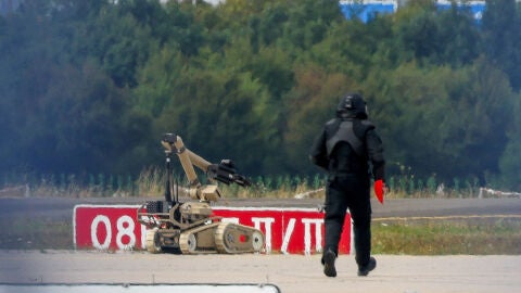 Un agente de polic&iacute;a con traje de protecci&oacute;n camina junto a un robot desactivador de explosivos (EOD) en Leipzig.