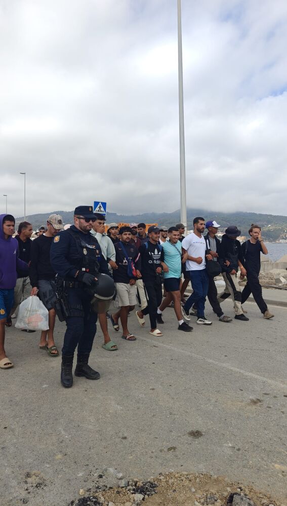 Un grupo de migrantes se agarra durante el traslado a uno de los espacios habilitados por el Gobierno en Ceuta.