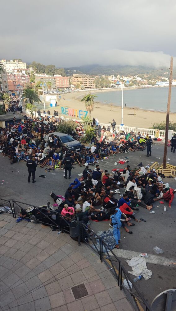 Decenas de migrantes aguardan ser trasladados desde playa Benítez al nuevo campamento habilitado por el Gobierno en Ceuta. 