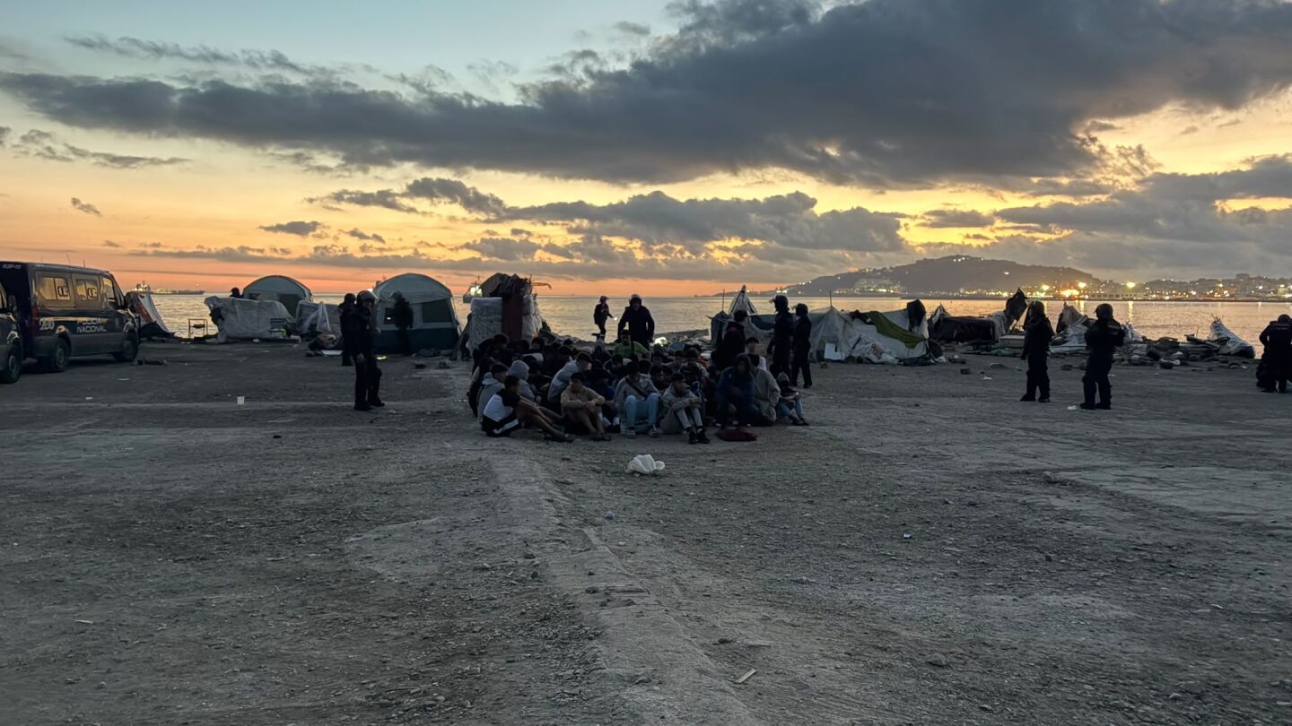 Migrantes agrupados por la Polic&iacute;a esperan a su traslado en la playa de El Guano