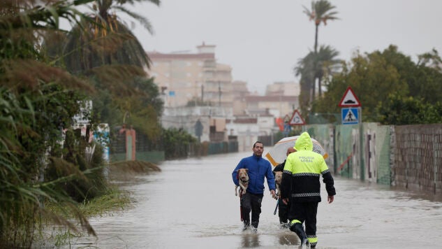 Un polic&iacute;a local se acerca a dos personas que abandonan la zona de la playa de Bellreguard (Valencia) a trav&eacute;s de una calzada inundada este lunes.