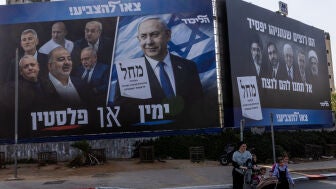 Varias personas caminan junto a una pancarta de campa&ntilde;a del partido Likud de Netanyahu antes de las elecciones parlamentarias en Israel