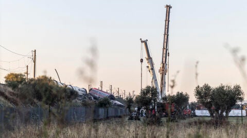 Los servicios de emergencia junto a maquinaria pesada trabajan en el lugar del accidente ferroviario un d&iacute;a despu&eacute;s del suceso